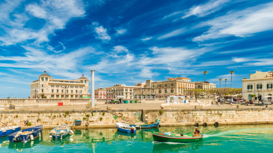 A motorboat sailing along the canal in Ortygia. Cityscape of the famous Sicilian town, Italy.