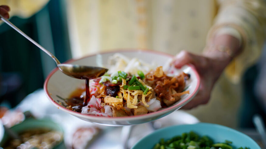 Merchant cook soy sauce on top of delicious Chinese steamed rice noodle rolls, beautifully arranged in white plate ready to serve customer in local restaurant.
